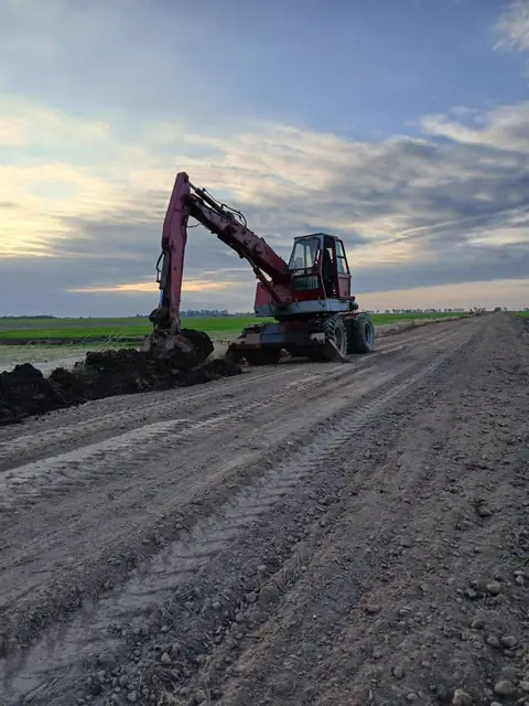 Excavadora abriendo una zanja al costado de un camino rural