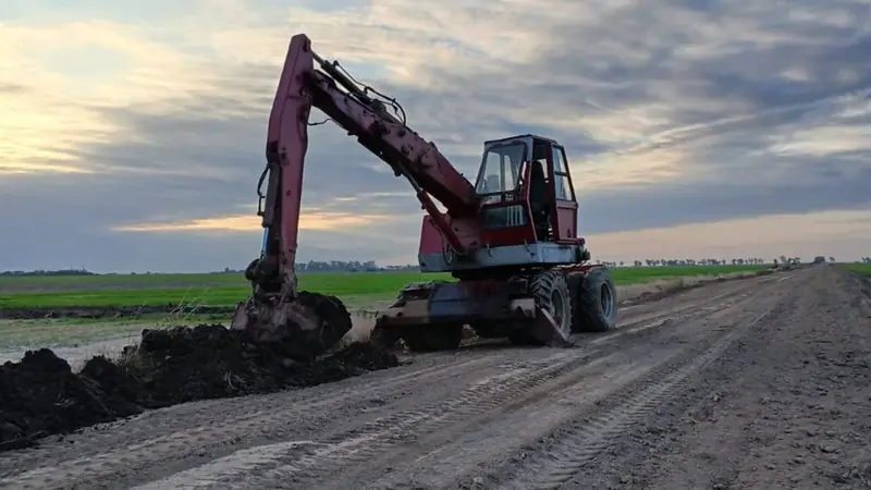 Excavadora abriendo una cuneta al costado de un camino rural